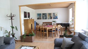 A living room with a sofa, coffee table, and a dining area with a table and chairs. There are plants and artwork on the walls. - Haus Gretchen Alpen (Alpen)