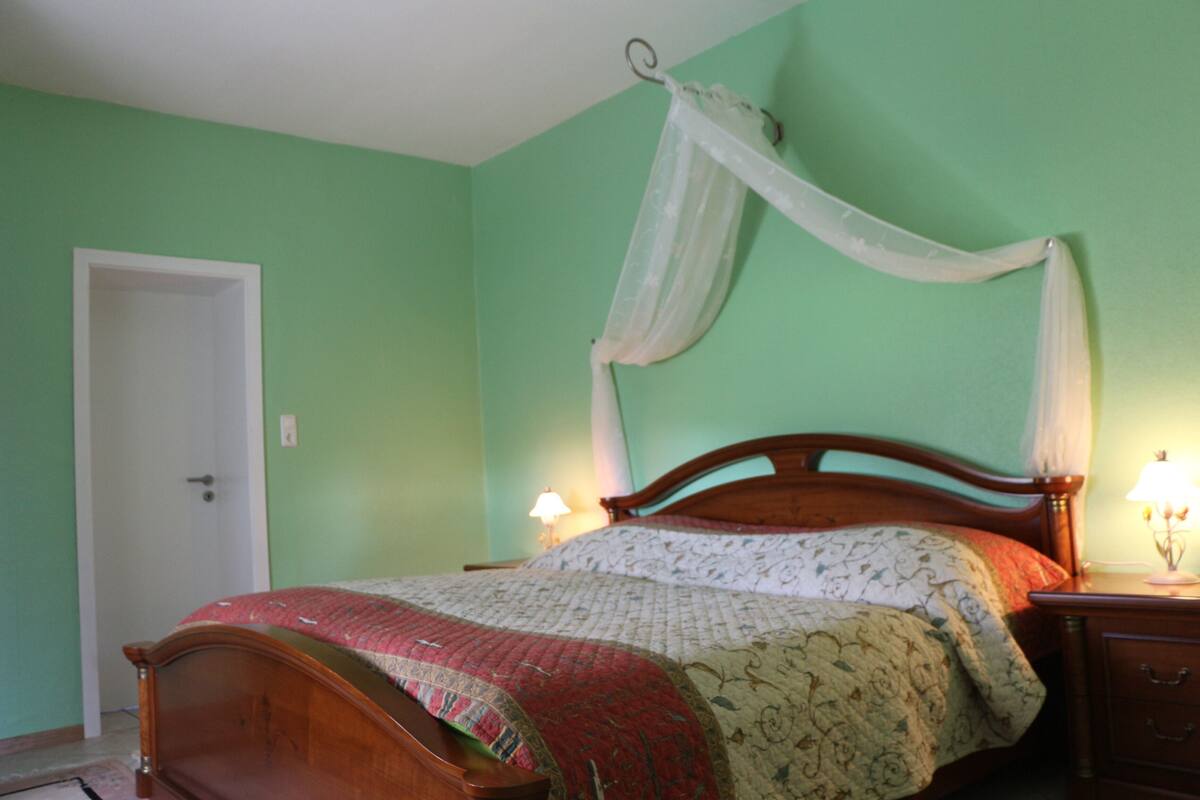 A bedroom with a wooden bed, a white door, and a nightstand with a lamp.