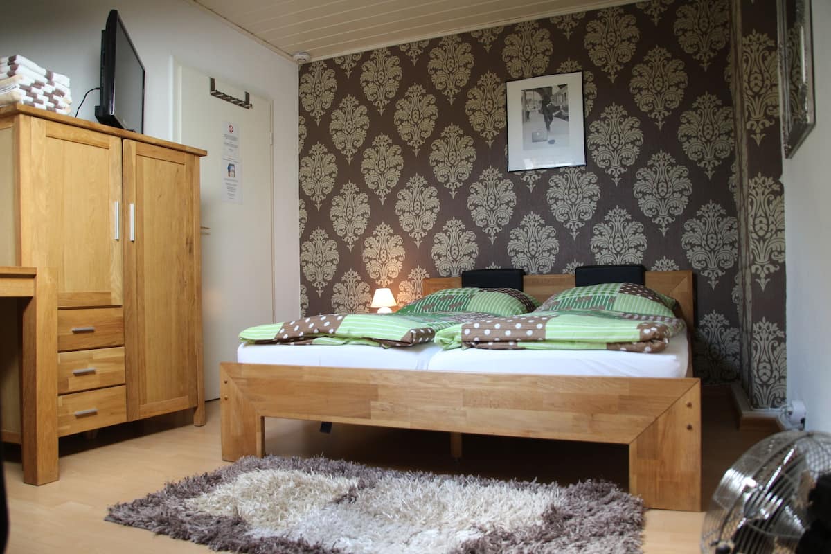 A bedroom with a wooden bed, a wooden wardrobe, a fluffy rug, and patterned wallpaper.