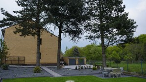 A building with a brick exterior, a small outdoor seating area with tables and chairs, and a well-maintained lawn. - Haus Gretchen Alpen (Alpen)
