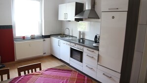A compact kitchen with white cabinets, a built-in oven, a stainless steel sink, and a window providing natural light. - Haus Gretchen Alpen (Alpen)