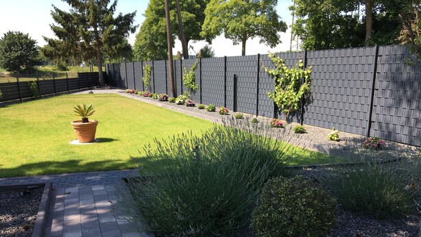 A landscaped garden with a paved walkway, a variety of plants, and a tall fence. - Haus Gretchen Alpen (Alpen)