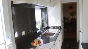 A kitchen with a granite countertop, a stainless steel sink, and a bowl of fruit. - Haus Gretchen Alpen (Alpen)