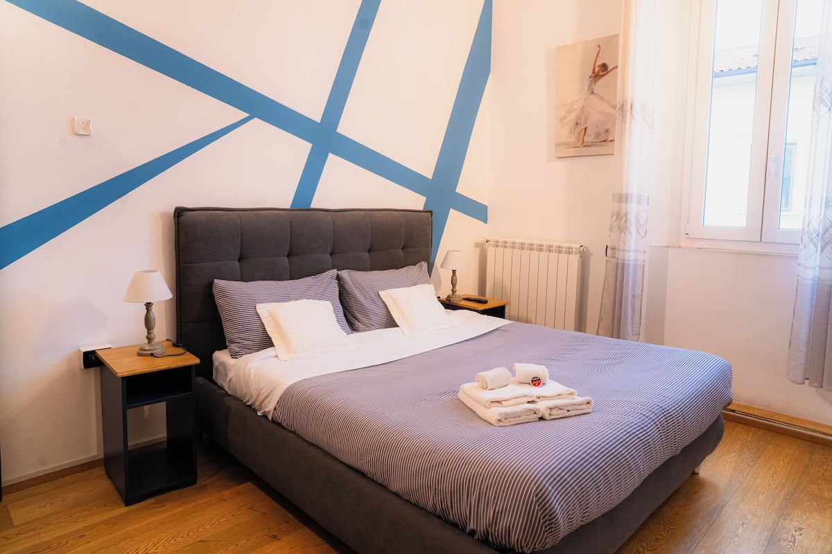 A bedroom with a bed, nightstand, lamp, and a painting on the wall.