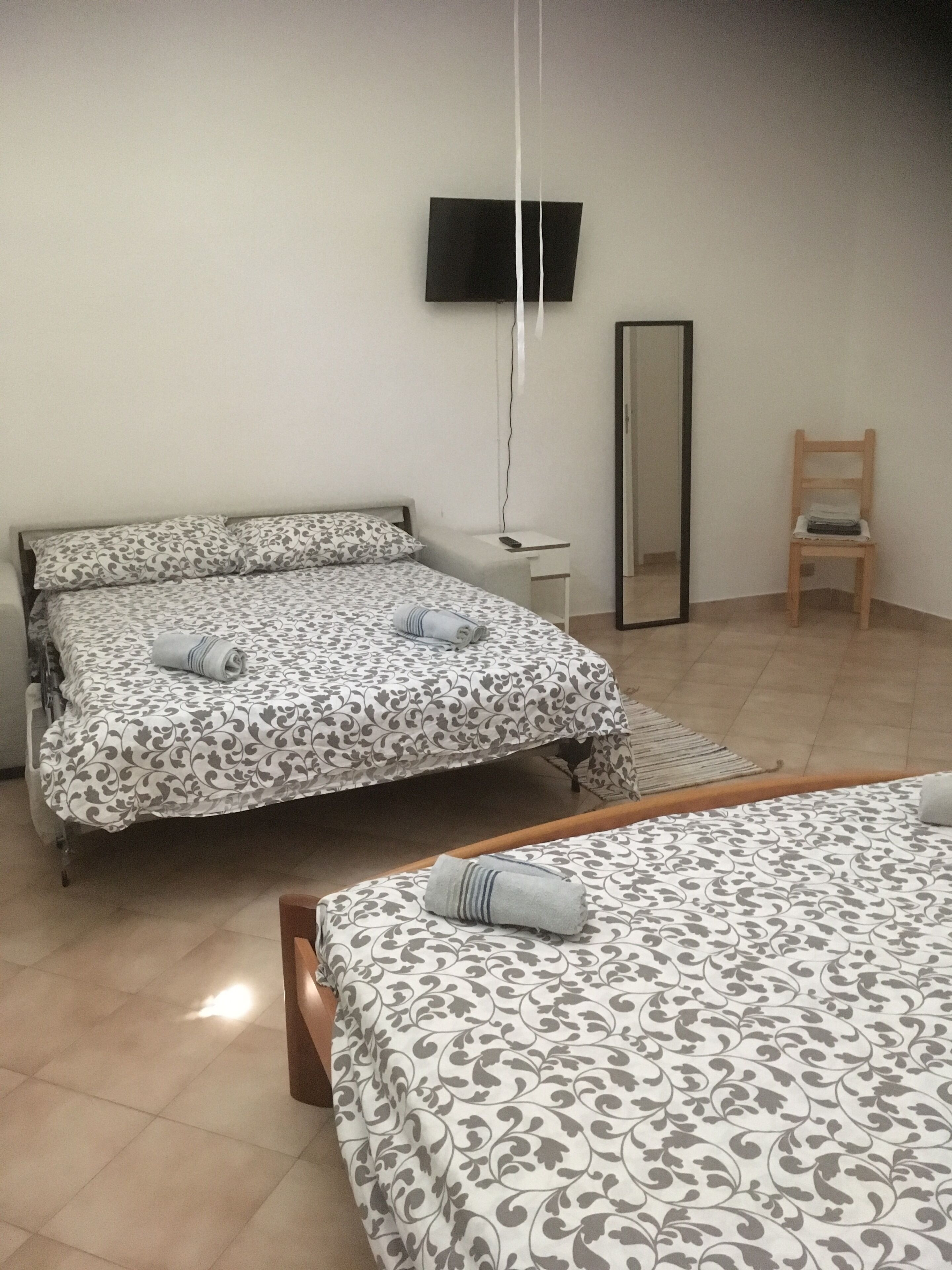 A bedroom with two beds, a TV mounted on the wall, a chair, and a small table.