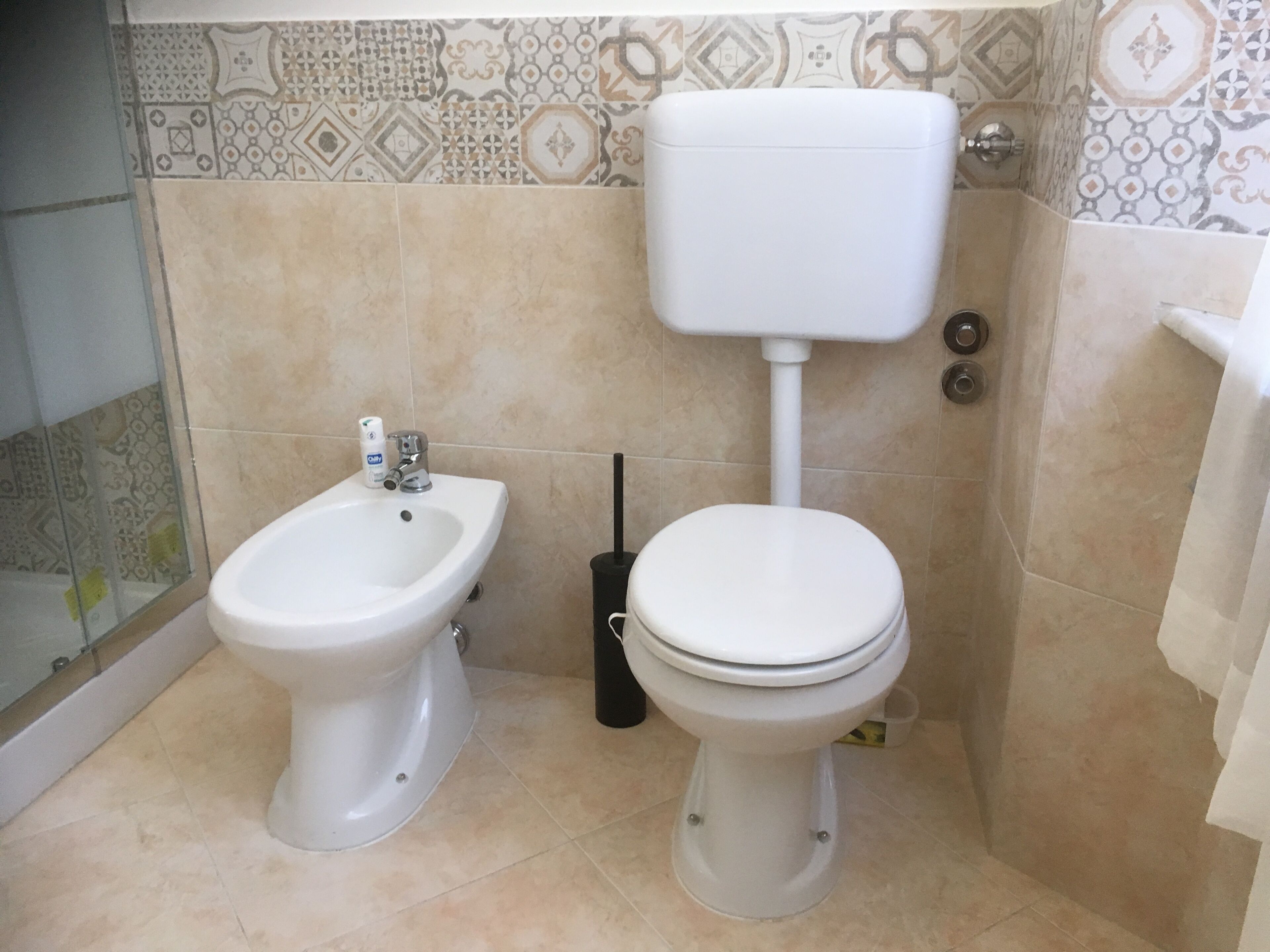 A bathroom with a bidet, toilet, and a wall-mounted toilet paper holder.