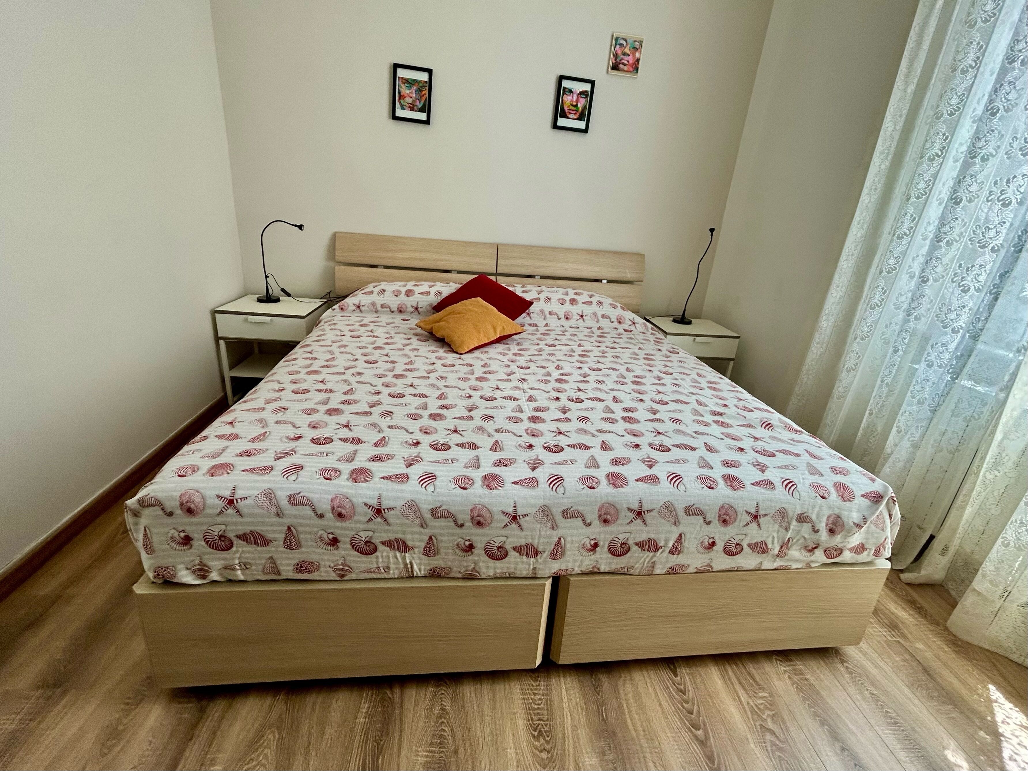 Un letto rifatto con cura, coperto da una trapunta fantasia, con una testiera in legno e due comodini con lampade.