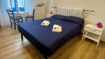 Un lit bien fait, avec deux serviettes pliées, une table de chevet avec une lampe et une chaise avec une petite table et une plante.