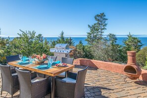 Un espacio exterior para comer con vista al mar, equipado con sillas de mimbre y una mesa dispuesta para una comida.