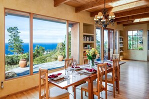 A dining area with a table set for four, large windows offering a view of the ocean, wooden beams on the ceiling, and a chandelier. - 3794 Forever Views II - Expansive Ocean Views (Carmel)