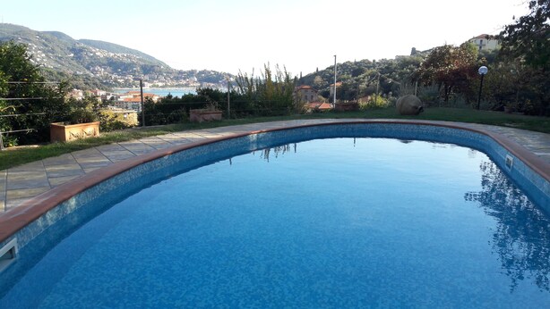 A swimming pool with a clear view of a hillside and buildings in the background. - Villa Sofia: apartments for short term holidays. (Lerici)