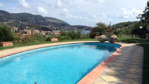 A swimming pool with a clear blue water, surrounded by a stone deck and a view of a hillside town. - Villa Sofia: apartments for short term holidays. (Lerici)