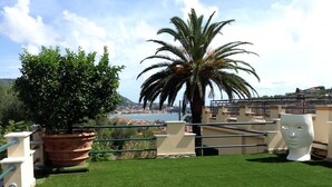 A rooftop terrace with a view of a coastal town, a palm tree, and a large planter with a tree. - Villa Sofia: apartments for short term holidays. (Lerici)