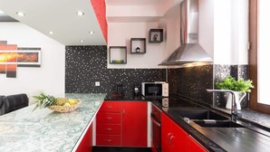 A modern kitchen with red cabinetry, a black backsplash, and a central island with a fruit bowl.