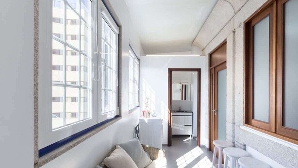 A narrow hallway with a sofa and bar stools, large windows, and a kitchen area.