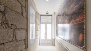 A corridor with stone walls, a door with a blue frame, and a large framed picture on the right wall.