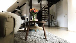 Una sala de estar con un sofá, una pequeña mesa de madera con un florero y un candelabro, además de una escalera.