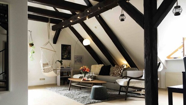 Un salón estilo loft con vigas de madera a la vista, un sofá, una mesa de centro y sillones colgantes de macramé.