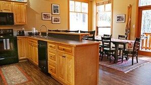 A kitchen with wooden cabinets, a central island, and a dining area with chairs and a table. - Perfect for larger groups, fantastic view to Red Mountain (Rossland)