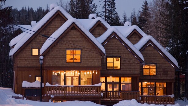 A wooden lodge with a snow-covered roof and a lit porch. - Perfect for larger groups, fantastic view to Red Mountain (Rossland)