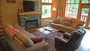 A cozy living room with a stone fireplace, a flat-screen TV, a sofa, a recliner, and a coffee table. - Perfect for larger groups, fantastic view to Red Mountain (Rossland)
