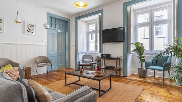 A living room with a sofa, coffee table, and chairs. There is a TV mounted on the wall and a plant on the floor. - LV Premier Baixa DO1 (Lisbon)