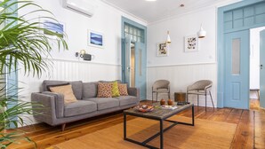 A living room with a grey sofa, a coffee table, and two chairs. There are two blue doors, a plant, and wall art. - LV Premier Baixa DO1 (Lisbon)