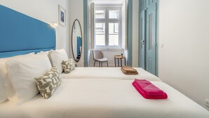 A hotel room with two beds, a chair, a small table, and a window with a view. - LV Premier Baixa DO1 (Lisbon)