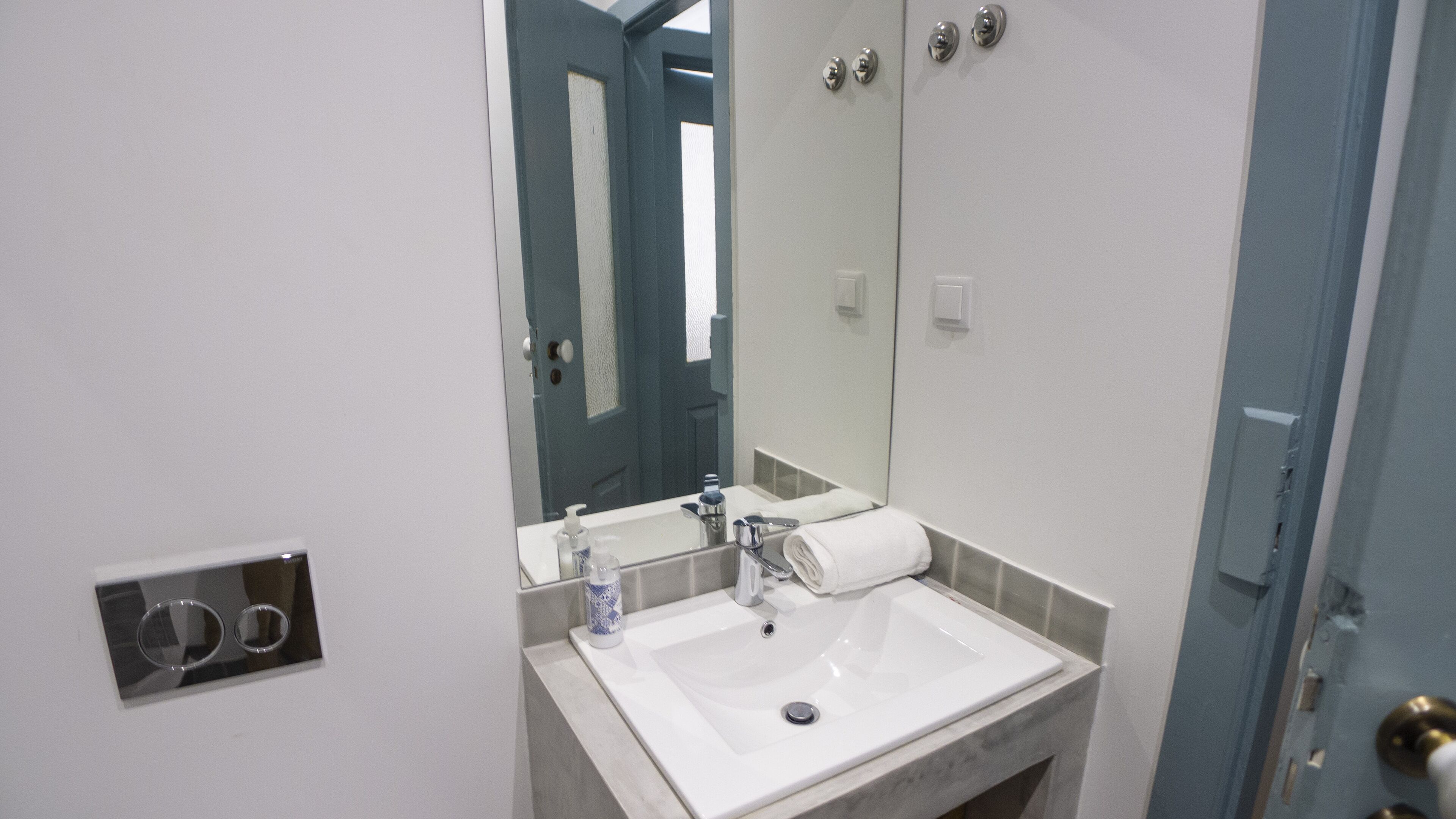 Une salle de bain avec un lavabo blanc, un miroir, une serviette et une porte.