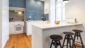 A modern kitchen with blue tiles, a central island with stools, and a window providing natural light. - LV Premier Baixa DO1 (Lisbon)