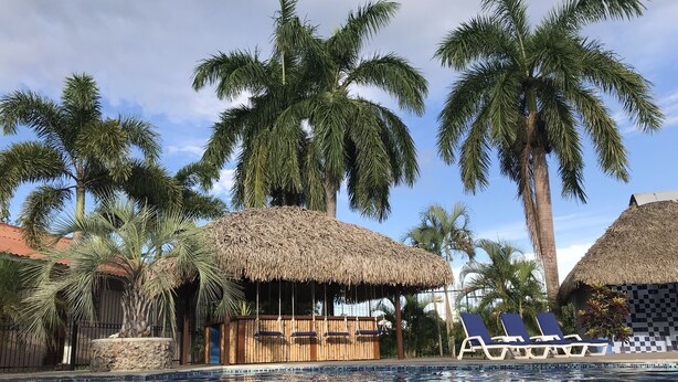 A swimming pool with a mosaic tile pattern, surrounded by palm trees and thatched-roof structures. - Luxury Poolside Apartment. Your Serene Getaway Awaits! (El Pajonal)