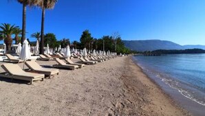 A beach with sun loungers and umbrellas, palm trees, and a clear blue sky. - Villa Onore - Luxurious pool jacuzzi (Dassia)