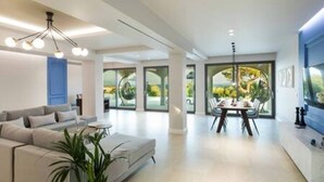 A modern living room with a sofa, coffee table, and a dining area with a table and chairs. - Villa Onore - Luxurious pool jacuzzi (Dassia)