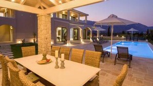 An outdoor dining area with a pool, stone pillars, and wicker furniture. - Villa Onore - Luxurious pool jacuzzi (Dassia)