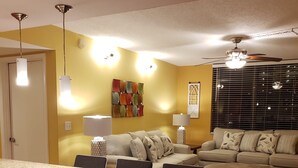 Una sala de estar moderna con comedor, paredes amarillas y un ventilador de techo.
