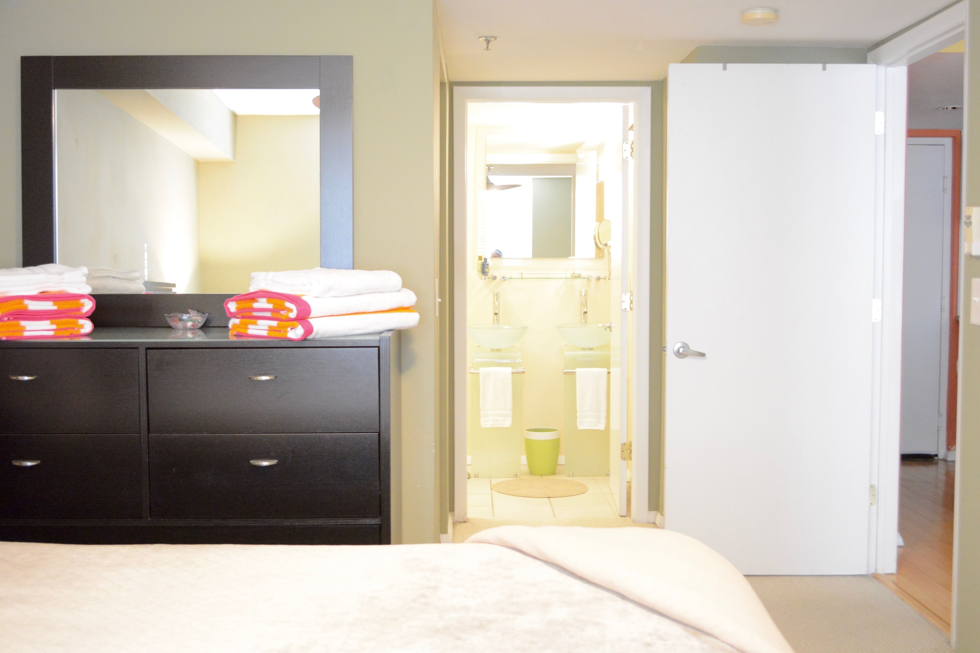A bedroom with a bed, a dresser with towels, a mirror, and a door leading to a bathroom.