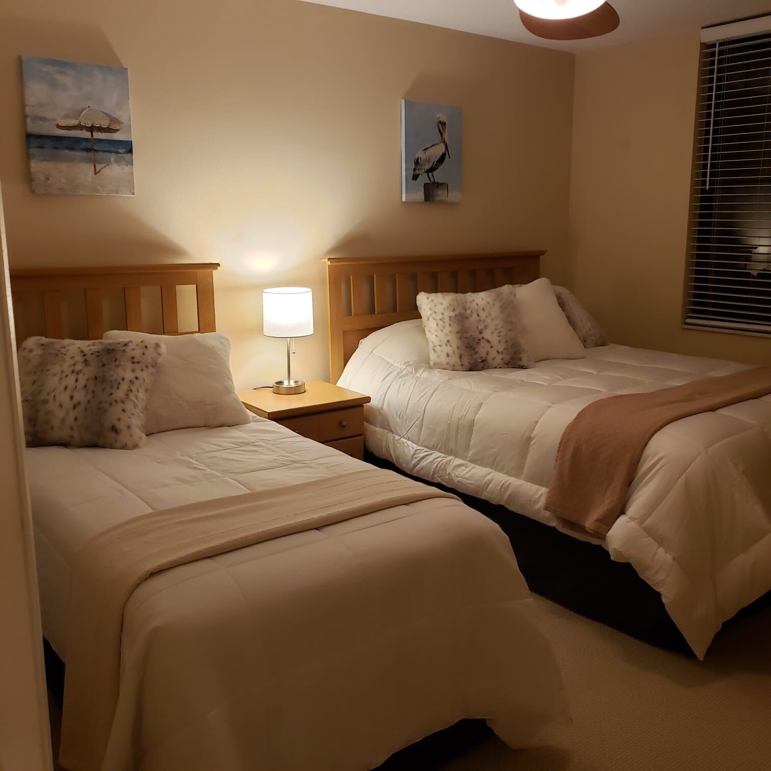 A hotel room with two beds, a nightstand with a lamp, and artwork on the walls.