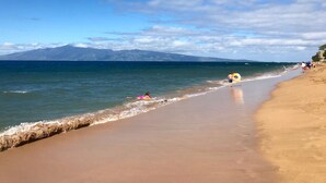 A beach with a clear sky, calm sea, and distant mountains.