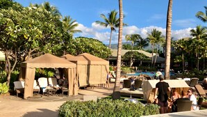 A resort pool area with lounge chairs, umbrellas, and palm trees.