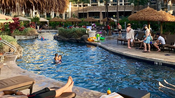 A resort pool area with lounge chairs, a water feature, and palm trees.