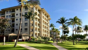 A multi-story hotel with balconies, a well-maintained lawn, and palm trees.