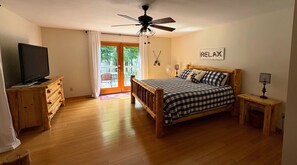 A bedroom with a bed, a television on a wooden dresser, a ceiling fan, and a 'RELAX' sign on the wall.
