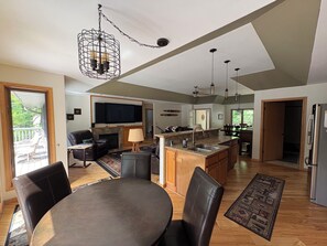 A spacious living area with a fireplace, a dining table with chairs, a kitchen with a large island, and a TV mounted on the wall.