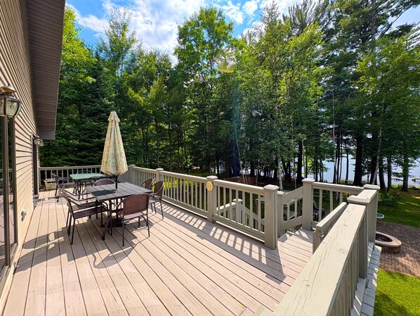 A wooden deck with outdoor furniture, a railing, and a view of a lake surrounded by trees.