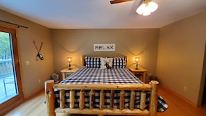 A bedroom with a checkered bedspread, two bedside tables with lamps, a ceiling fan, and a 'RELAX' sign on the wall.