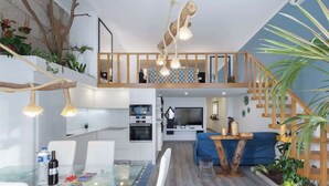 Un appartement moderne de style « loft », doté d’une table à manger en verre, d’un canapé bleu et d’une cuisine avec un téléviseur.
