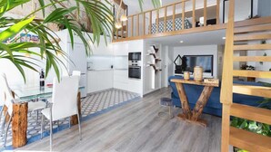 Une cuisine moderne avec des meubles blancs, une table à manger avec des chaises et un escalier en bois menant à l’étage supérieur.