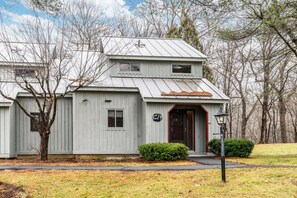 A two-story building with a dark front door, a small porch, and a metal roof. - Condo above Quechee Village with Golf Views, Windsor (Hartford)