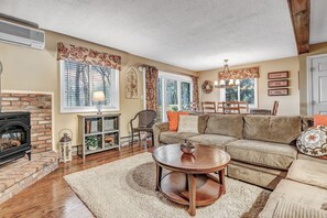 A living room with a fireplace, sofa, coffee table, and a dining area with chairs. - Condo above Quechee Village with Golf Views, Windsor (Hartford)