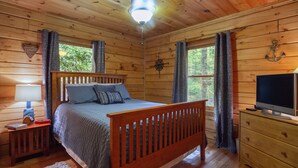 A wooden cabin bedroom with a bed, a TV, and a dresser.